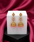 Gold and pink earrings on a white cube with a red fabric background