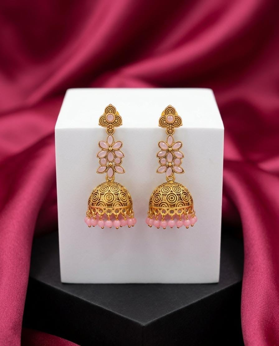 Gold and pink earrings on a white cube with a red fabric background